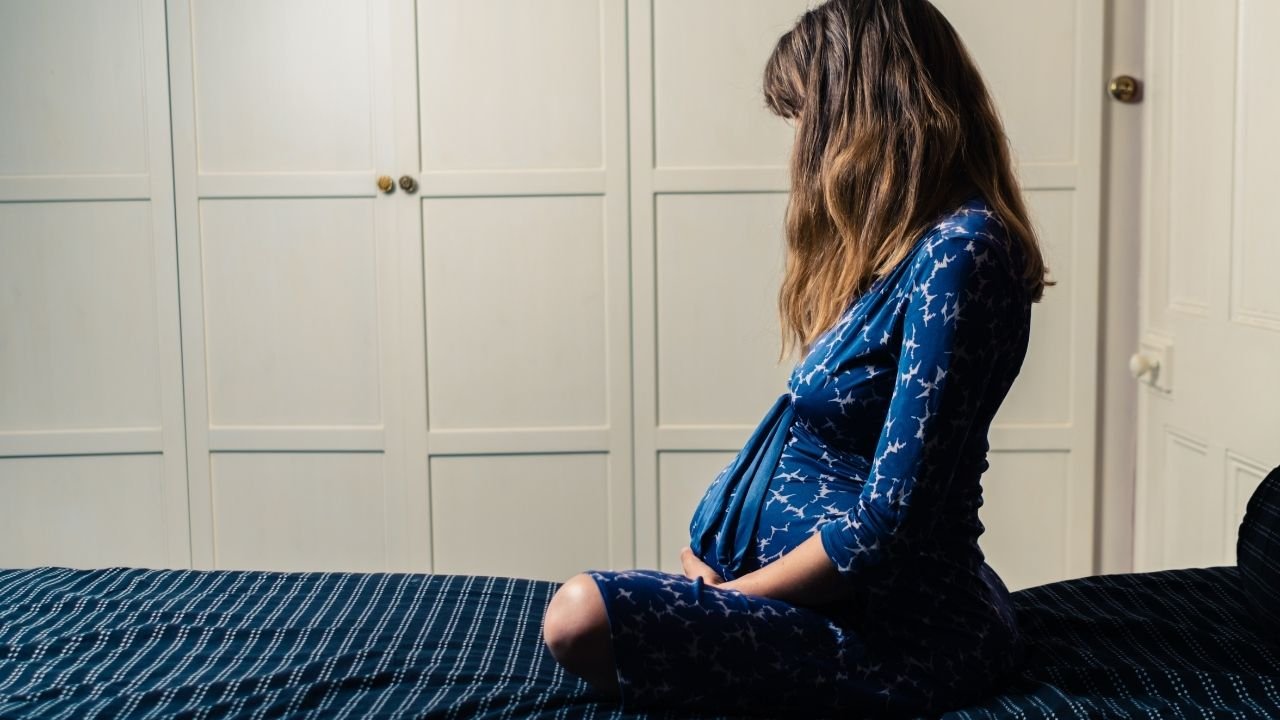 grávida sentada na cama com camisola estampada
